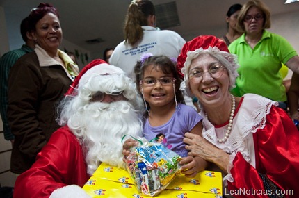 Santa Claus y su esposa junto a una feliz paciente recibiendo su regalo