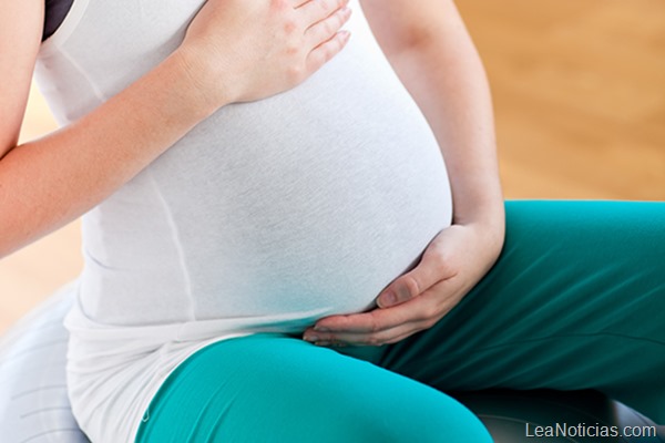 Young pregnant woman touching her belly sitting on a fitness ball