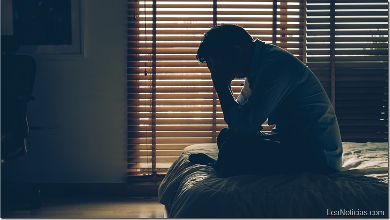 Sad businessman sitting head in hands on the bed in the dark bedroom with low light environment