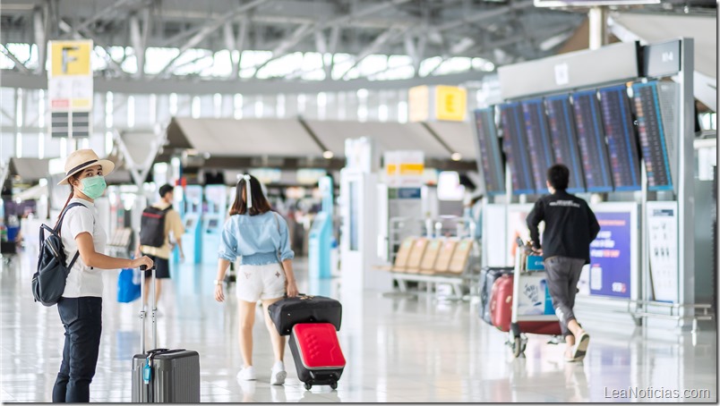 Young female wearing face mask with luggage walking in airport terminal, protection Coronavirus disease (Covid-19) infection, Asian woman traveler with hat. New Normal and travel bubble concept