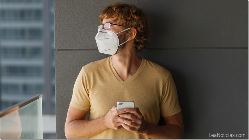White bearded adult man using smartphone while wearing surgical mask on an industrial wall. Health, epidemics, social media.